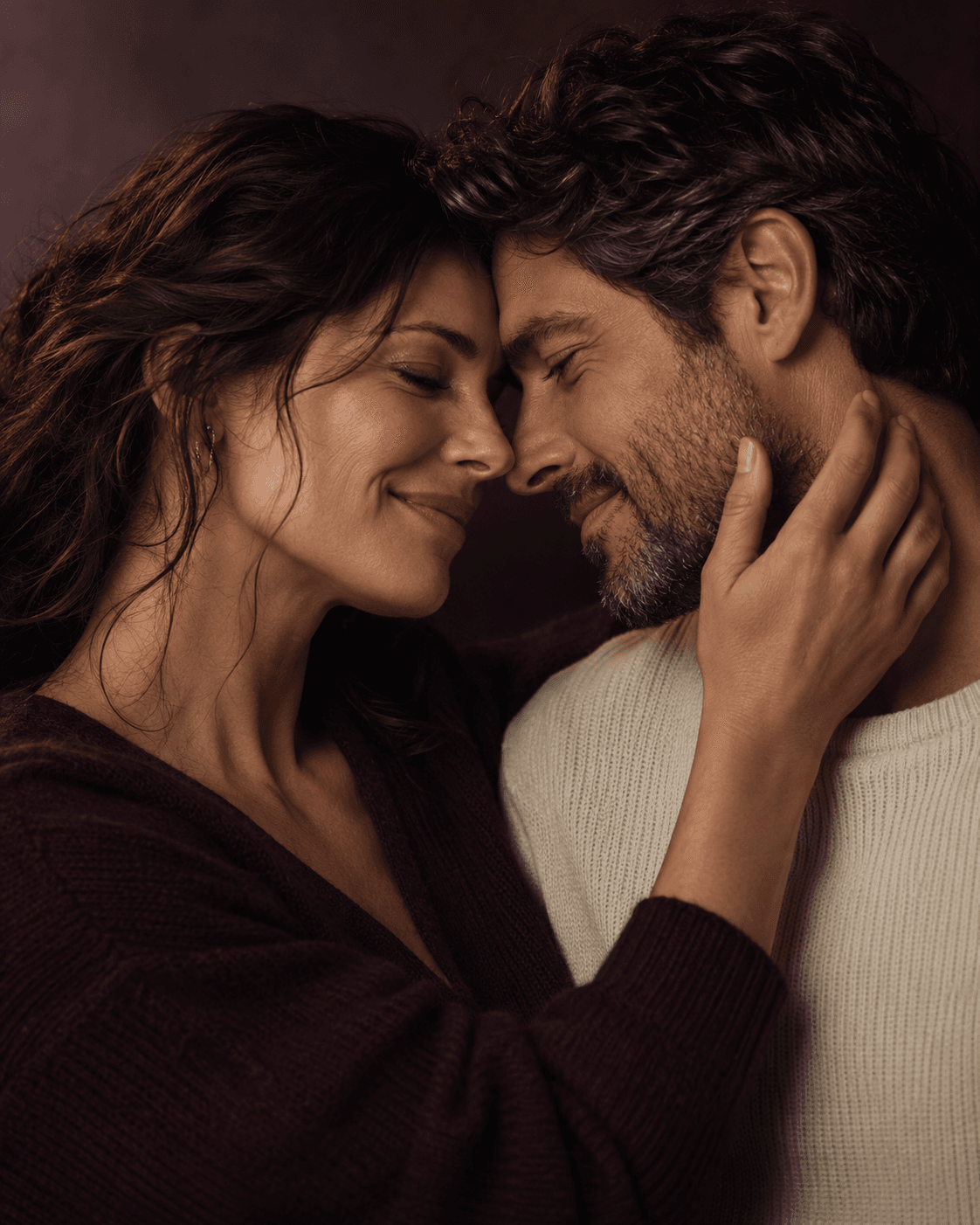 An adult couple, foreheads touching, one hand resting against a cheek.